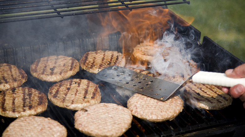 Person pressing burgers on a grill