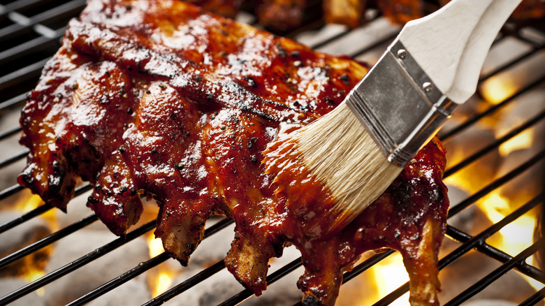 Person brushing barbecue ribs with sauce