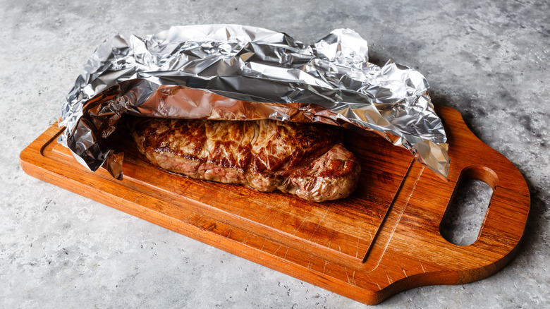 Grilled steak resting on a cutting board under tin foil