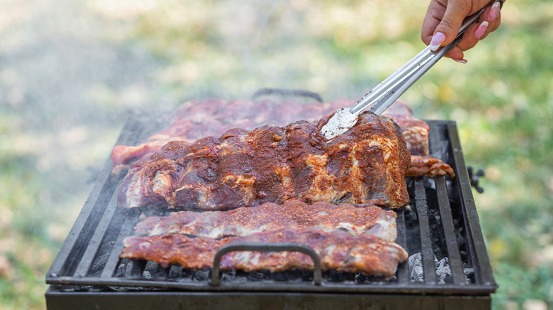 Person using tongs to flip ribs on a grill