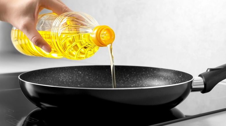 Hand pouring oil into frying pan