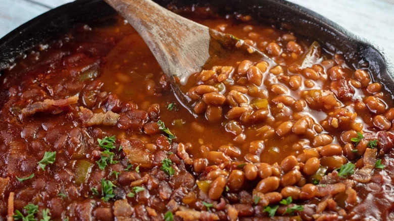 BBQ baked beans in a pan with a wooden spoon