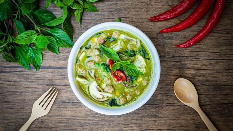 bowl of Thai green curry with basil, chilis and utensils 