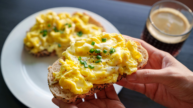 Hands holding scrambled eggs on toast