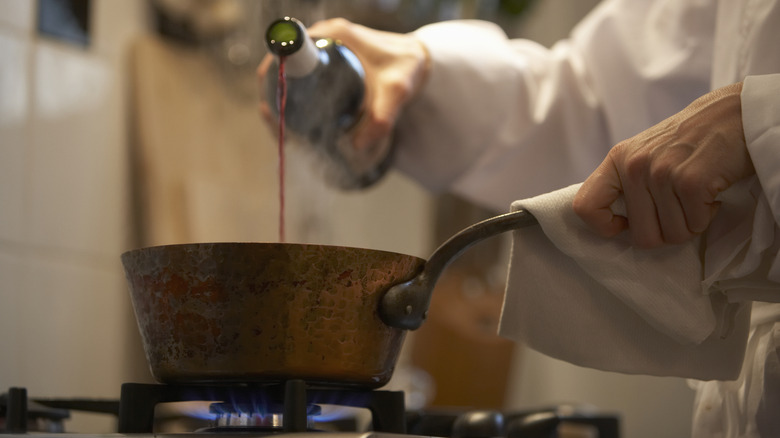 Person pouring red wine into pan