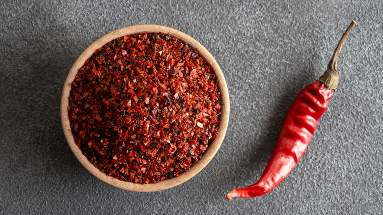 Red pepper flakes in bowl and dried chili pepper