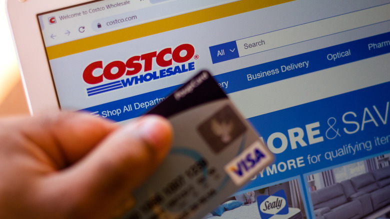 holding credit card in front of Costco website homepage