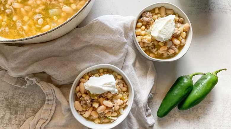 White turkey chili in a pan and bowls with sour cream with peppers