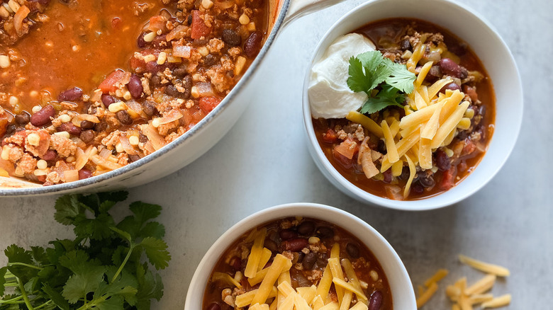 Turkey chili in a pan and bowls with cheese and sour cream