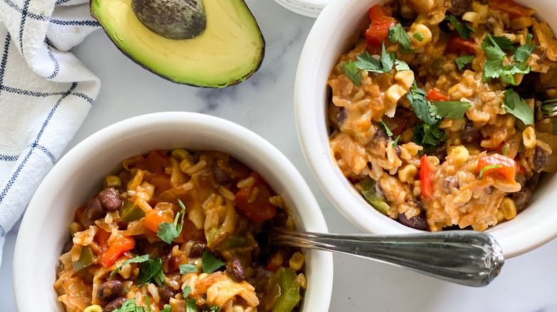 An avocado next to two white bowls filled with stovetop enchiladas