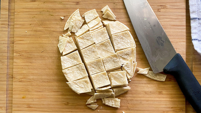 A knife and cut up tortillas on top of a wooden cutting board