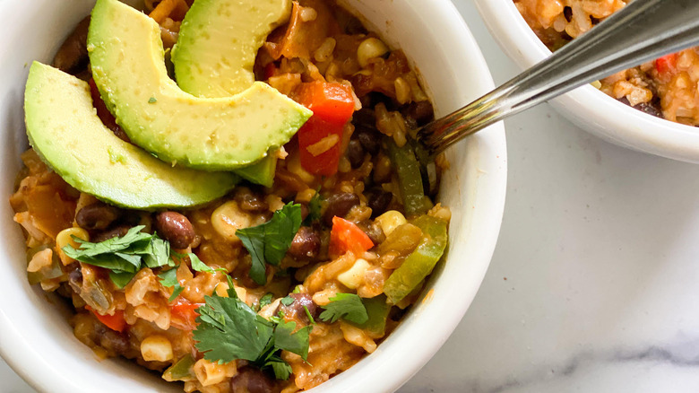 Overhead shot of a white bowl filled with stovetop enchiladas and topped with slices of avocado