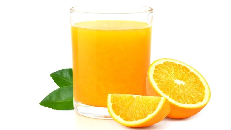 A short glass of orange juice with a cut orange on the side