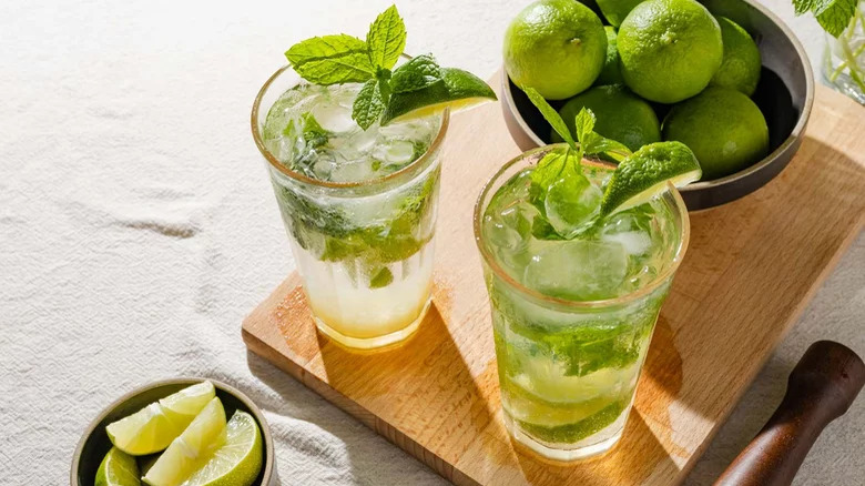 Two mint mojitos next to a bowl of limes