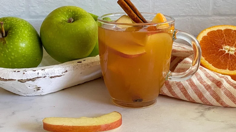 glass mug of apple cider, with whole green apples behind it