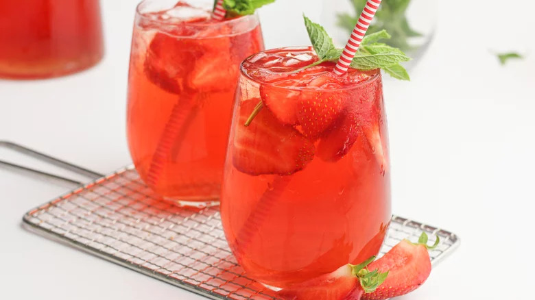 Two stemless wine glasses with red, strawberry-based beverage, garnished with mint leaves