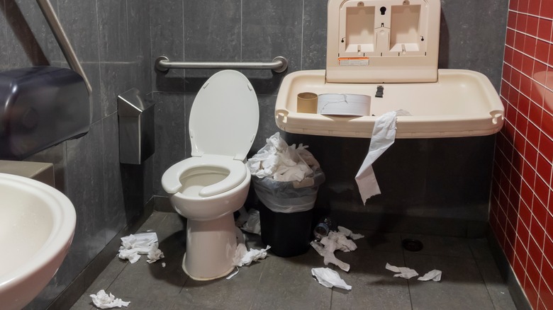 a dirty restroom with tissue on the floor