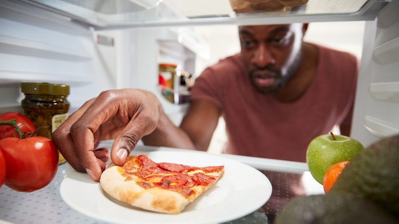 Man takes leftover pizza from fridge