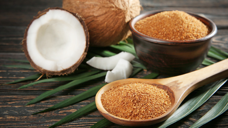 coconut sugar in bowl and spoon with palm fronds and coconuts in background