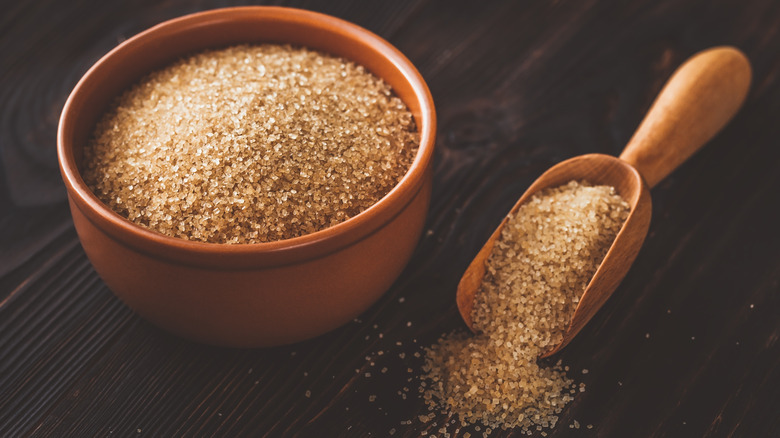 raw sugar in bowl and scoop on wooden background