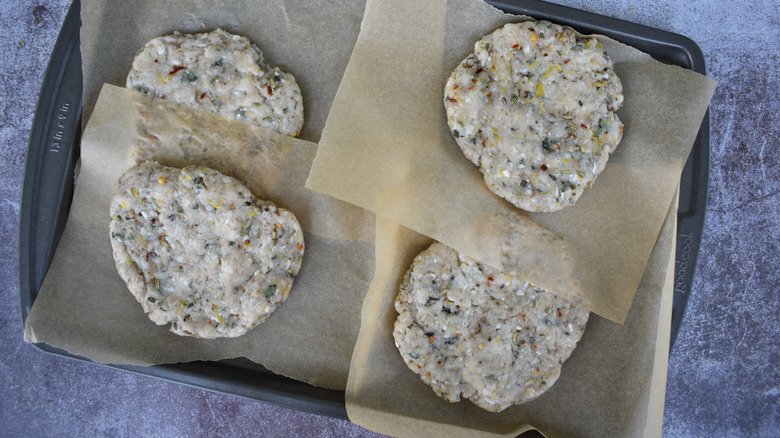 raw chicken burger patties on wax paper on a metal tray