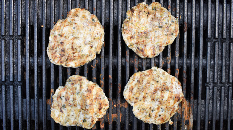 four chicken burger patties grilling on a grill