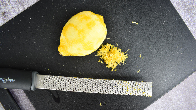 zested lemon sitting next to a zester on a black board