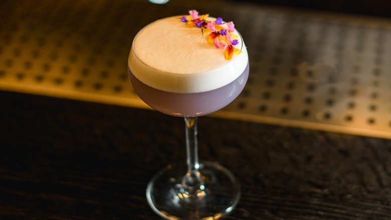 Purple cocktail with egg white froth and edible flowers