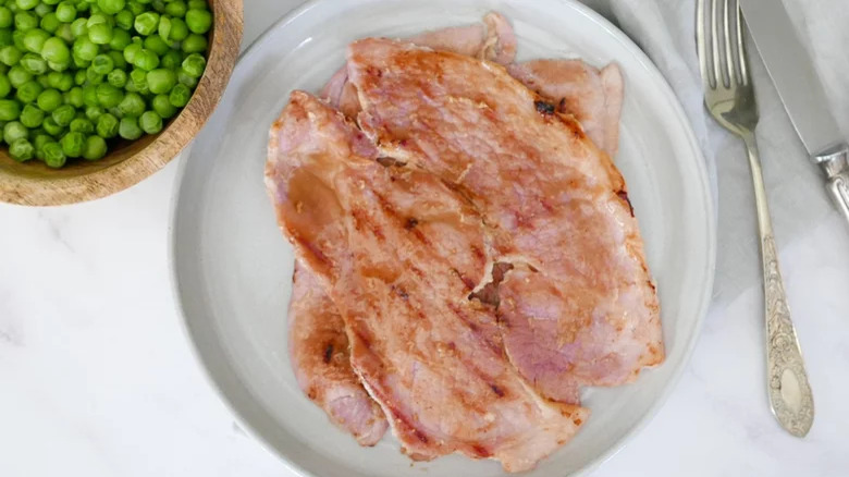 Honey mustard ham steak on a plate with peas in a bowl