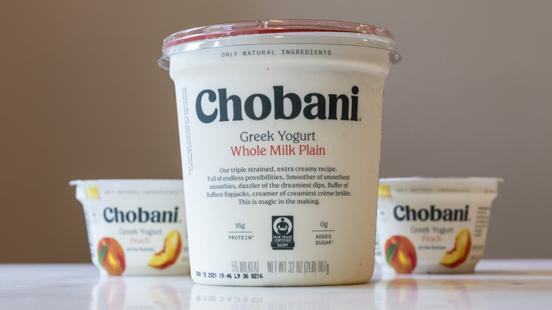 A carton of Chobani's Whole Milk Plain Yogurt, along with two cups of peach flavored yogurt