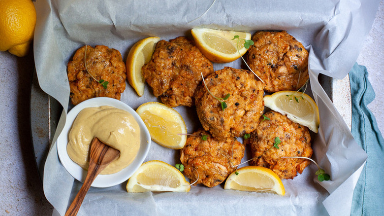 Fried salmon patties with lemon wedges and herbs on tray.