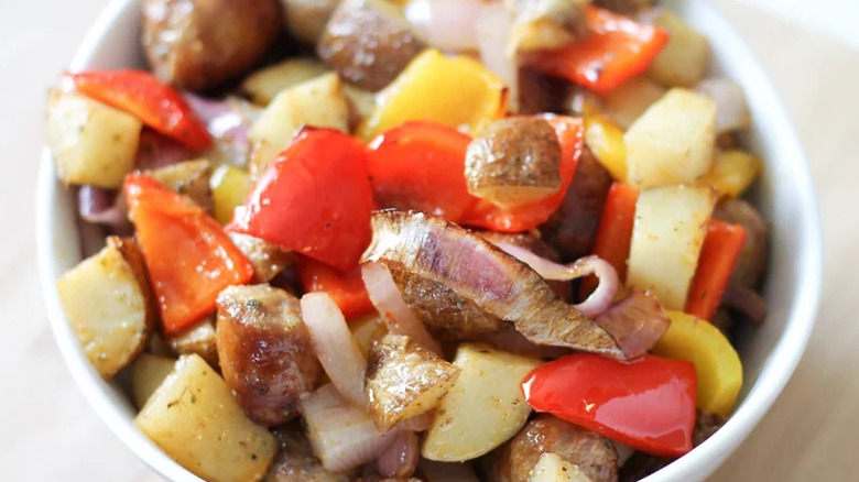 White bowl with sautéed potatoes, peppers, and sausage.