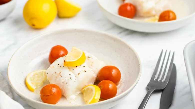 White dish with cooked cod, lemons, and cherry tomatoes.