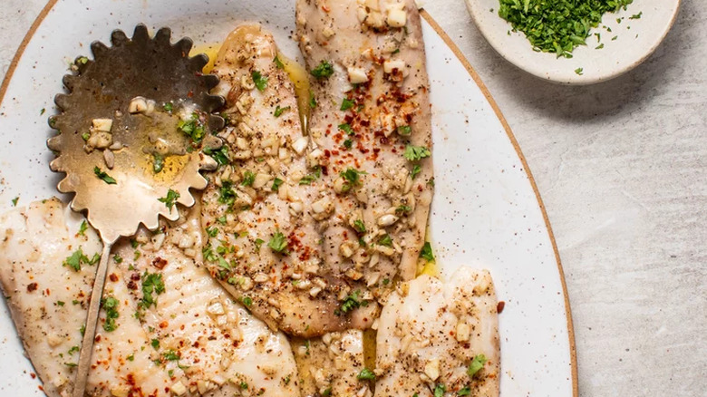 Baked fish filets with garlic on platter with scalloped spoon.