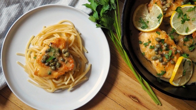 Chicken with caper sauce over noodles on a plate. 