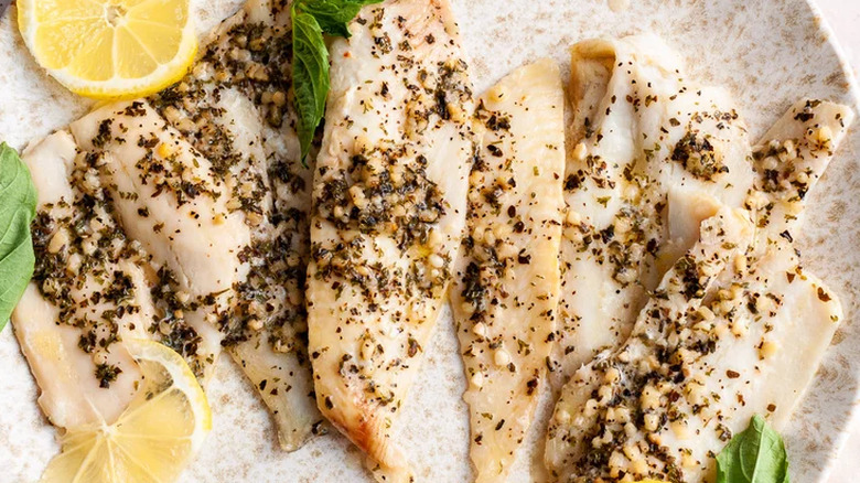 Cooked pieces of fish with garlic herb blend and lemon slices.