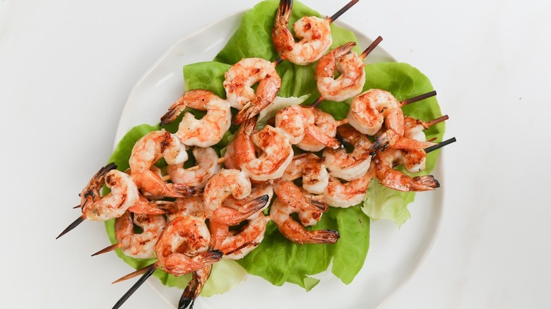 Skewers of grilled shrimp on a bed of lettuce.