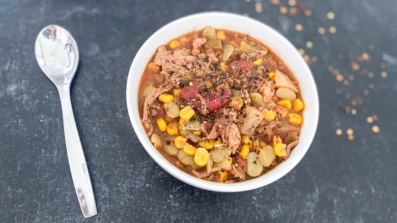 Bowl of meat, corn, and lima bean stew with spoon.