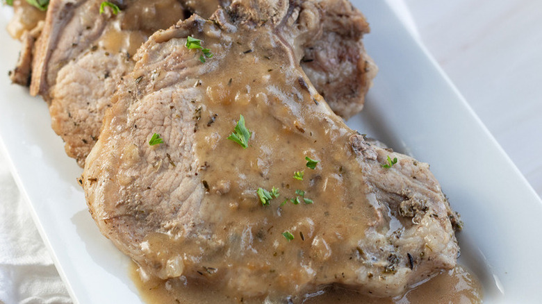 Cooked pork chops on platter with gravy and herbs.