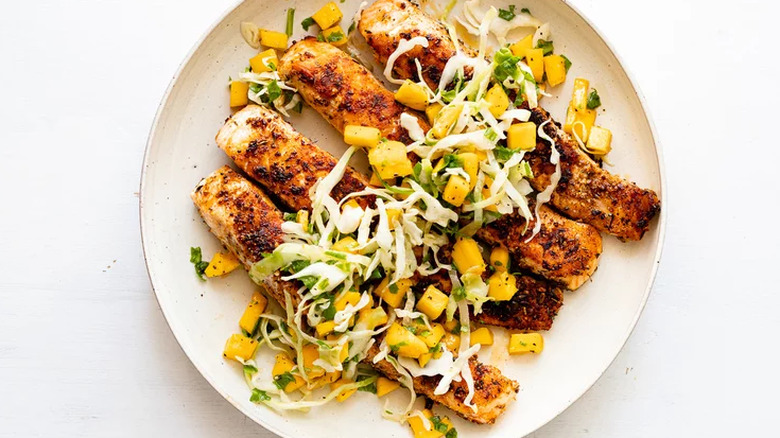 Strips of seasoned fish with mango and greens.