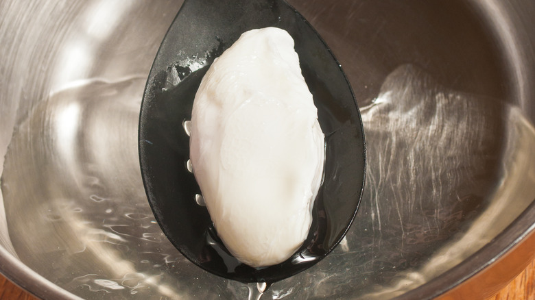 A poached egg being picked up by a slotted spoon