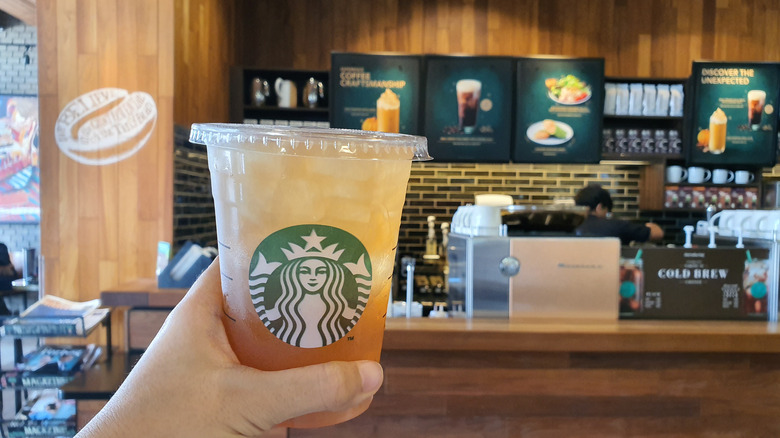 Hand holding lemonade in front of Starbucks sign