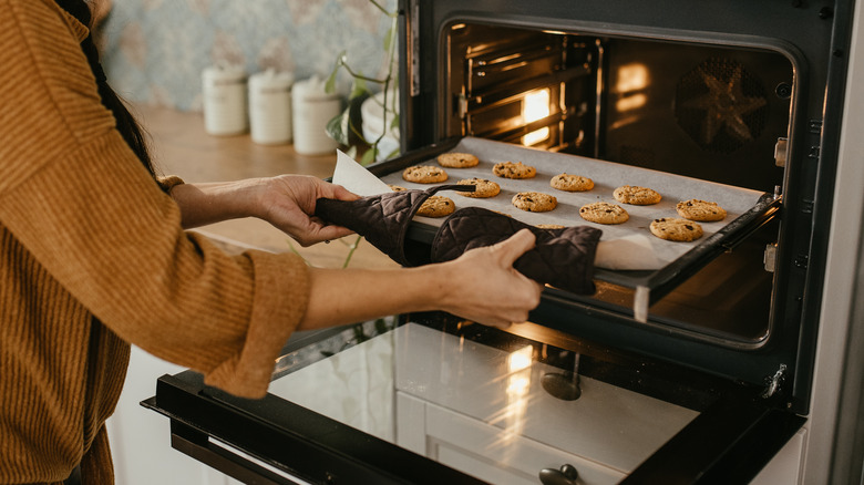 Woman taking tray of cookies out of oven