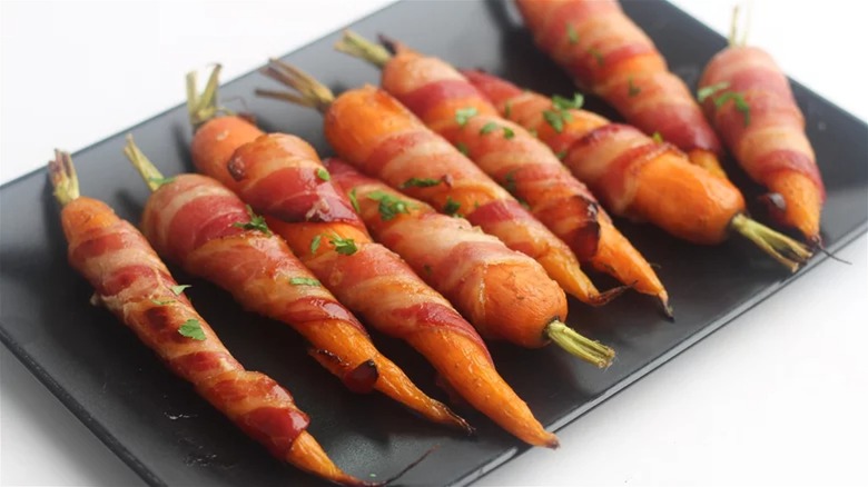 Row of carrots wrapped in bacon on rectangular dish