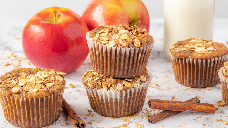 Oat-topped brown muffins with apples and cinnamon sticks.