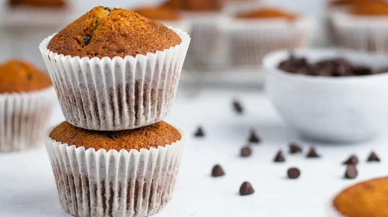 Two pumpkin muffins stacked with chocolate chips on table.