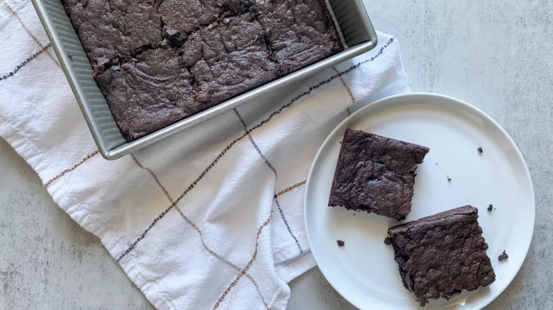 Pan of brownies with two pieces on a plate.
