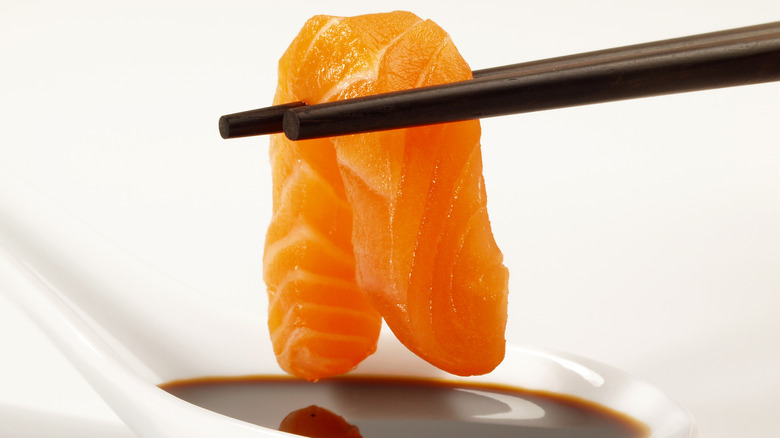 Salmon sashimi above dipping bowl of soy sauce