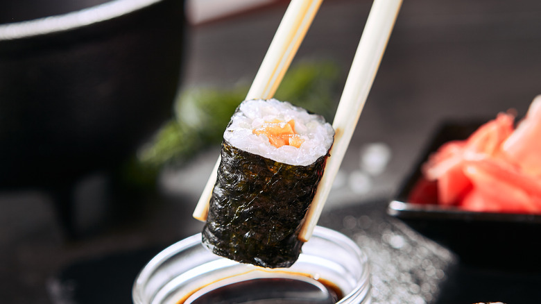 Chopsticks dipping salmon maki in soy sauce