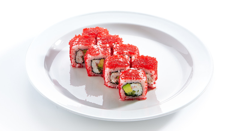 Red tobiko caviar around maki sushi roll on white plate